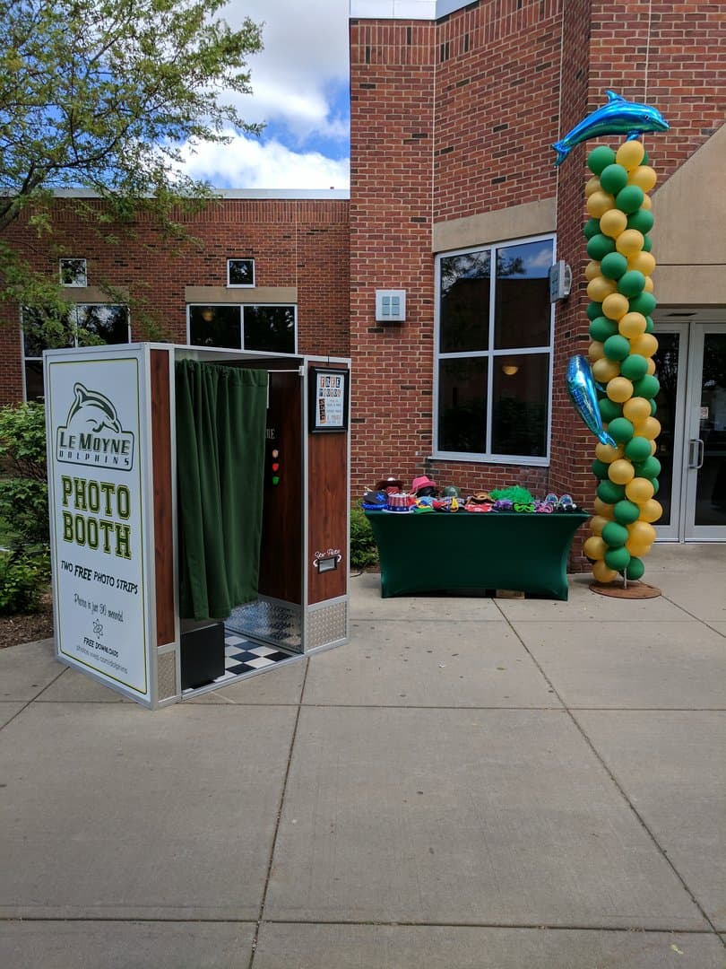 Photo booth set up outdoors beside a skirted prop table loaded with hats, glasses, and signs